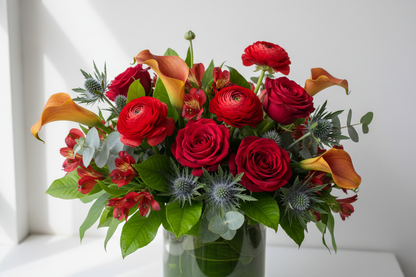 flower arrangement with mango callas, lemon leaf, red ranunculus, red roses, green thistle, red astrolumeria, eucalyptus, in cylinder vase